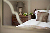 Brown cushion and lamp with vintage chest of drawers at bedside in Petworth farmhouse West Sussex Kent