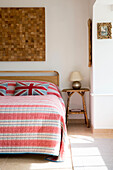 Gestreifter Bettbezug und Holzschnitt-Kunstwerk mit Beistelltisch in einem Haus in West Wittering, West Sussex, England