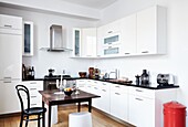 Weiße Einbauküche mit Holztisch und rotem Mülleimer in einem modernen Londoner Einfamilienhaus England UK