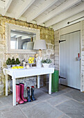 Rectangular mirror above table with wellington boots in flagstone entrance hallway of UK farmhouse