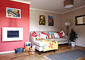 Rote Wand mit Print-Kollektion und bunten Kissen im Wohnzimmer eines Hauses in Bolton, Greater Manchester, England, UK
