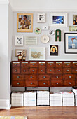 Assorted artwork above vintage wooden sideboard with stacked magazines in London home  UK