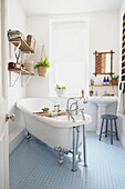 Freestanding bathtub at sash window in blue floored bathroom of Sheffield home  Yorkshire  UK