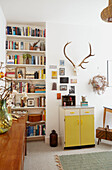 Antlers above yellow cupboard with bookshelf in London home  UK