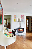 Dog stands with pair of cream chairs and lit woodburner in York home  England  UK