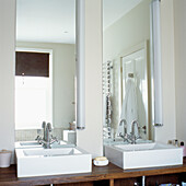 Nahaufnahme eines modernen Badezimmers mit zwei weißen Waschbecken in maßgefertigten Schränken aus dunklem Walnussholz vor langen Spiegeln