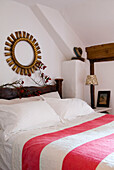 Bedroom with red and white striped bedspread and a round gilt frame hangs above branches of red berries on the bedhead