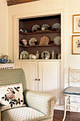 Antique china collection in recessed alcove with armchair and floral patterned cushion 