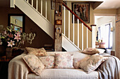 Holzbalken und Treppe im Cottage-Wohnzimmer mit cremefarbenem Sofa und blumengemusterten Kissen