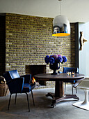 Dining area with leather armchair and vase of blue and purple hydrangeas on a round table against a brickwork chimney breast with open fire