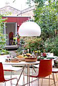 White pendant light hangs over garden table set with fruit and bread