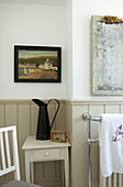 Badezimmer mit feuchtigkeitsresistenten, schilfgetäfelten Wänden, antikem Spiegel und Krug auf dem Tisch unter dem Kunstwerk