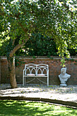 Cushions on a metal garden seat with bust in walled garden