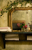 Cut flowers on wall shelf with salvaged mirror and climbing rose