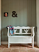 Ampersand on panelled wall with artwork above salvaged garden bench painted white in Suffolk family home England UK