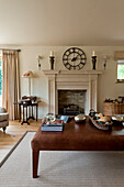 Roman clock on fireplace with brown leather ottoman footstool in Canterbury home England UK
