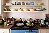 Kitchenware and utensils on open shelving with kettle on oven in London home UK