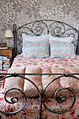 Vintage metal bed with quilts and metallic floral wallpaper in bedroom of London home UK