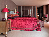 Red velvet bed cover and metallic side unit in bedroom of London apartment England UK