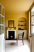 View through double doors to yellow room with recessed shelving in rural Suffolk home England UK