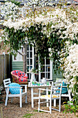 Painted table and chairs under flowering blossom in back garden of London home, UK