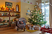 Weihnachtsbaum und Schaukelstuhl mit Regalen in einem Familienhaus in Forest Row, Sussex, England, UK