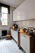 White fitted kitchen with child's chair and blackboard in Paris apartment, France