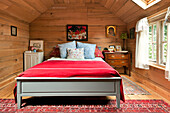 Red woollen blanket on double bed in wood clad bedroom of Essex home, England, UK