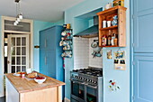 Holzinsel mit wandmontierten Regalen in blauer Küche eines Einfamilienhauses in Bovey Tracey, Devon, England, UK