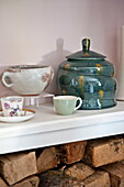 Hand painted ceramics with firewood on shelf in Bovey Tracey family home, Devon, England, UK