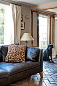Black leather sofa with animal print cushion in living room of Suffolk farmhouse, England, UK