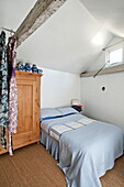 Double bed with wooden wardrobe and dresses in attic bedroom of Suffolk farmhouse, England, UK