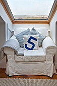 White slip cover on armchair at window of attic bedroom in Wadebridge home, Cornwall, England, UK