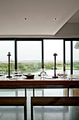 Esstisch aus Holz mit Sitzbänken und Blick auf die Landschaft aus einem modernen Einfamilienhaus, Cornwall, England, UK