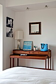 Photographs and mirror above wooden table in bedroom of contemporary home, Cornwall, England, UK