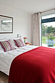 Rote Wolldecke auf einem Doppelbett mit gestreiften Kissen in einem modernen Haus, Cornwall, England, UK