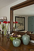 Schnittblumen und Ornamente auf Sideboard mit holzgerahmtem Spiegel in modernem Landhaus in Suffolk, England, UK