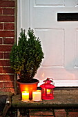 Kerzen und immergrüne Topfpflanze vor der Tür eines Cottages in Shropshire, England, UK