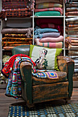 Gehäkelte Decken und Kissen auf einem abgenutzten Ledersessel mit Regalen voller walisischer Decken in einem Geschäft in Tregaon, Wales UK