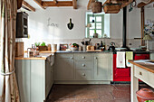 Light green fitted kitchen with small window and flagstone flooring in Sherford barn conversion Devon UK
