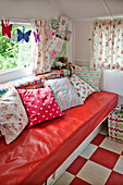 Verschiedene Kissen mit geblümten Vorhängen und Schmetterlingsdekoration über einer roten Sitzbank in einem Wohnwagen