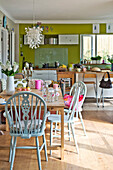 Gestrichene Stühle am Holztisch in einer lindgrünen offenen Küche in einem Einfamilienhaus in East Grinstead, West Sussex, England, UK