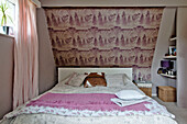 Mustertapete über einem Doppelbett mit rosa Decke und Vorhängen in einem Einfamilienhaus in East Grinstead, West Sussex, England, UK