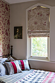 Roman blinds at window above bed with scarlet striped cushions in Stamford home Lincolnshire England UK