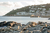Harbour wall and fishing village of Mousehole viewed from rocky peninsular Cornwall UK