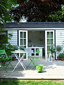 Table with green folding chairs on decking of UK summerhouse and work studio