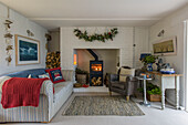 Armchair and sofa at lit wood burning stove in Penzance farmhouse Cornwall UK