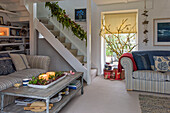 Beleuchtete Kerzen auf einem Couchtisch mit gestreiften Sofas in einem offenen Wohnzimmer mit Treppe in einem Bauernhaus in Penzance, Cornwall, Großbritannien