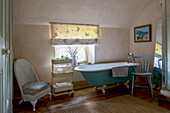 Freestanding turquoise bath with chairs and service trolley at window in Helston farmhouse Cornwall UK