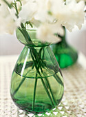 Detail of green glass vase on tabletop with white cut flowers